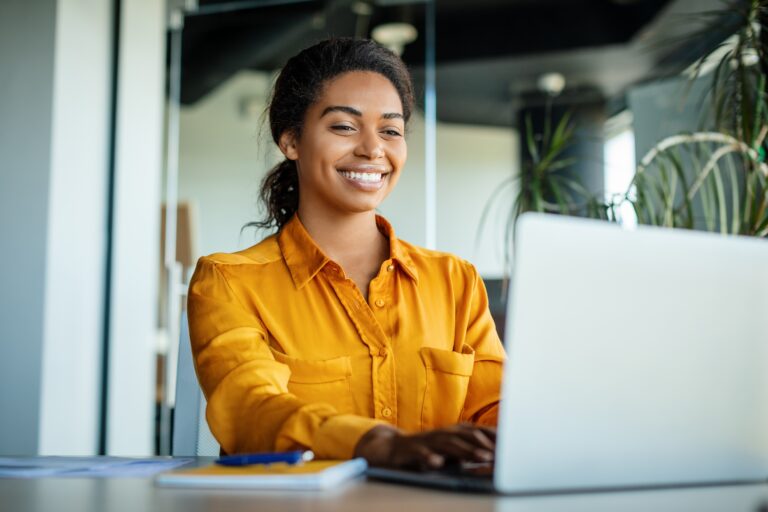 Happy black accounts payable professional using laptop and working efficiently with her ERP and AutoVouch while sitting at her in-office desk.