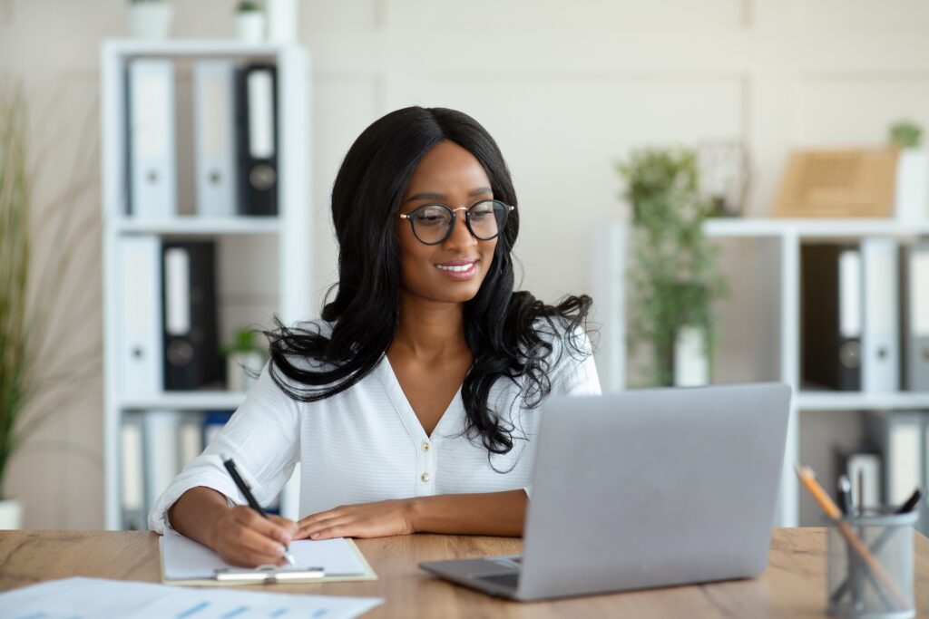 Cheerful business woman working on a laptop, taking notes on the step by step of how to automate accounts payable.