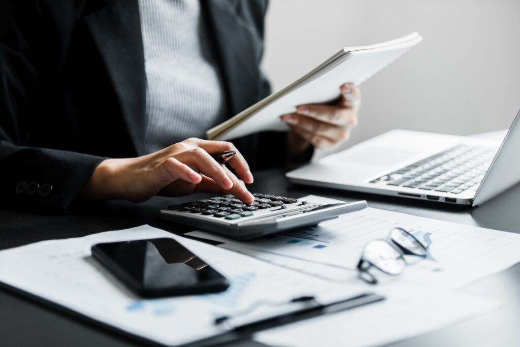 Woman at a desk, typing on a calculator, with paperwork in the background.