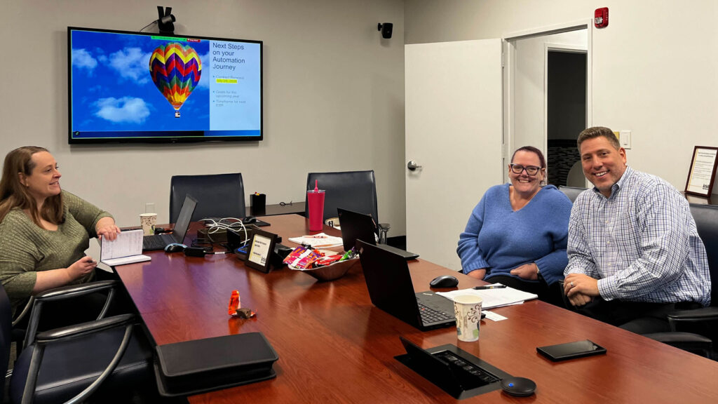 Business executives from Arbill and DataServ sit around a conference table while smiling