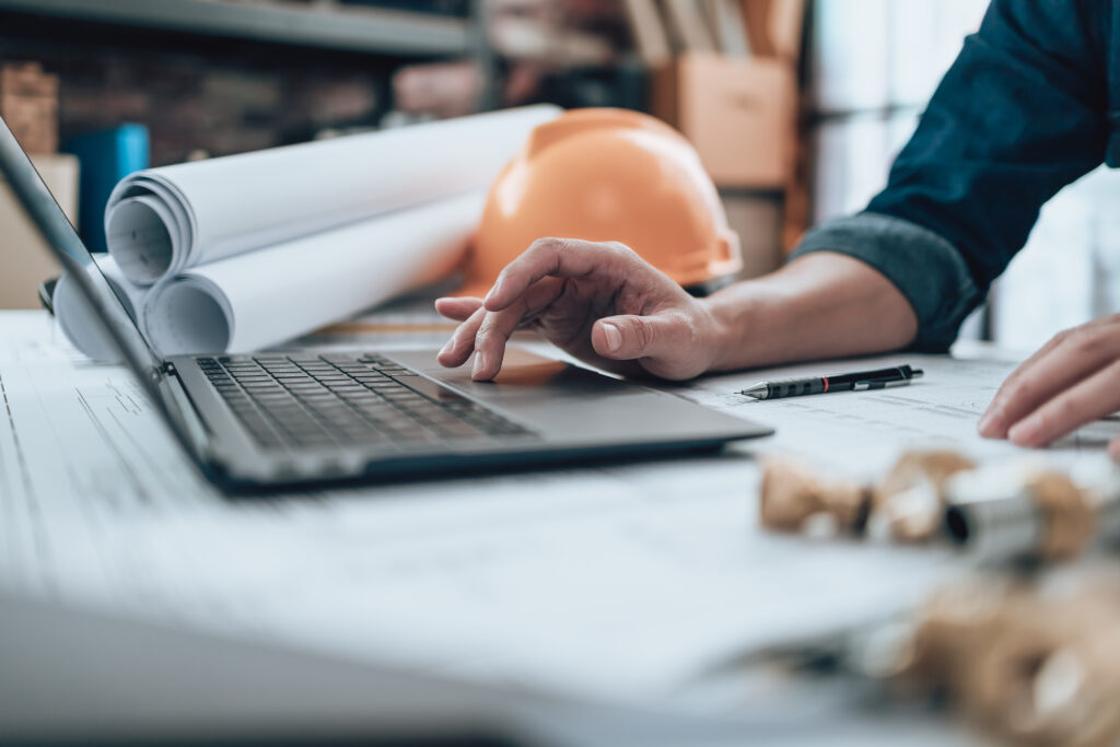 Engineering working with drawings inspection on laptop in the office and Calculator, triangle ruler, safety glasses, compass, vernier caliper on Blueprint. Engineer, Architect, Industry and factory concept.